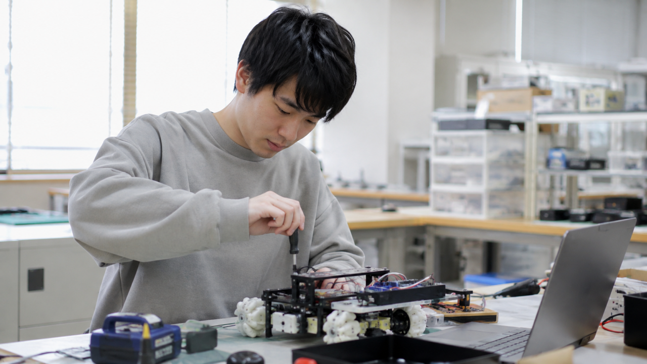 工学系の学生が実験室で小型ロボットを調整するイメージ